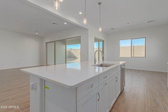 kitchen featuring an island with sink, stainless steel dishwasher, light wood-type flooring, sink, and decorative light fixtures