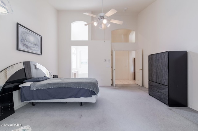 carpeted bedroom featuring a towering ceiling, arched walkways, and a ceiling fan