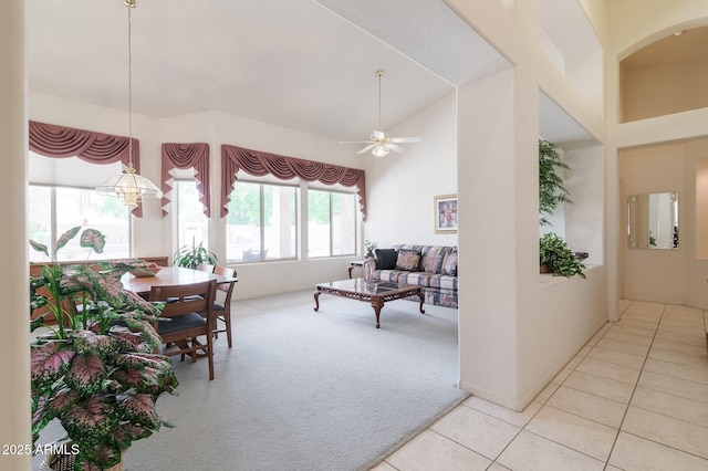 living area with high vaulted ceiling, light carpet, light tile patterned floors, a ceiling fan, and a chandelier