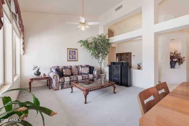 carpeted living area featuring ceiling fan and a towering ceiling