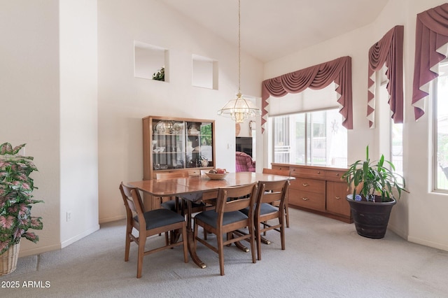 dining room featuring light colored carpet, a chandelier, baseboards, and high vaulted ceiling