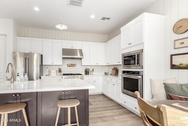 kitchen featuring visible vents, under cabinet range hood, a breakfast bar, and stainless steel appliances
