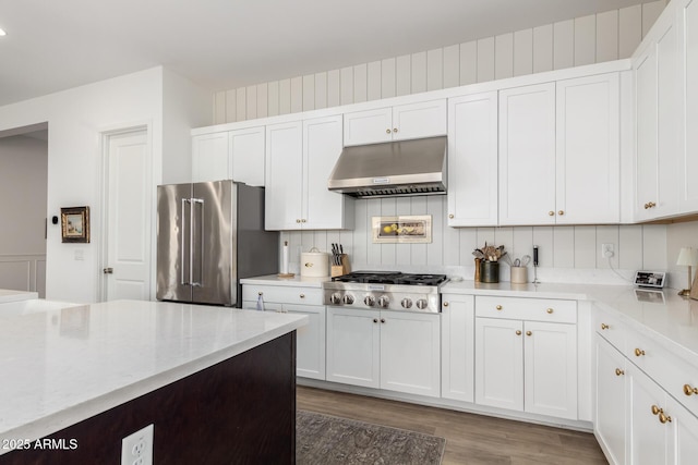 kitchen featuring under cabinet range hood, white cabinets, tasteful backsplash, light wood finished floors, and appliances with stainless steel finishes