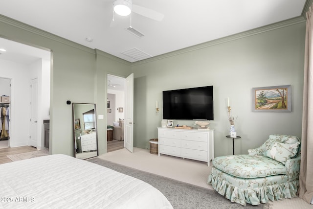 bedroom with crown molding, a walk in closet, a ceiling fan, and visible vents