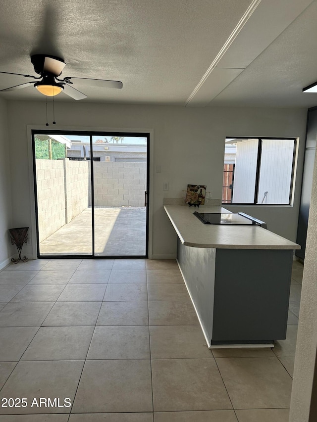 kitchen with light tile patterned flooring, black electric stovetop, ceiling fan, and a textured ceiling