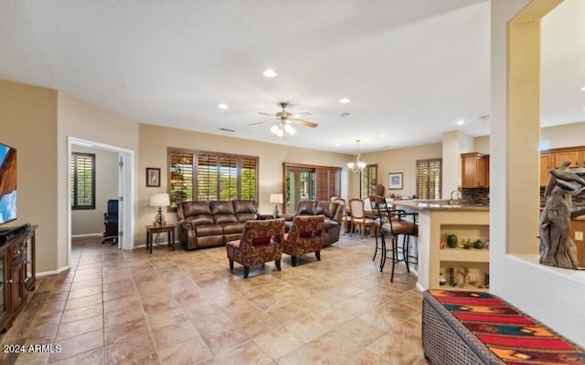 tiled living room featuring ceiling fan with notable chandelier and sink