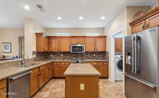 kitchen with a center island, sink, light stone counters, stainless steel appliances, and washer / dryer