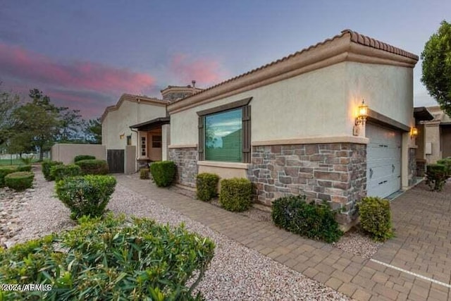 view of home's exterior with a garage, stone siding, decorative driveway, and stucco siding