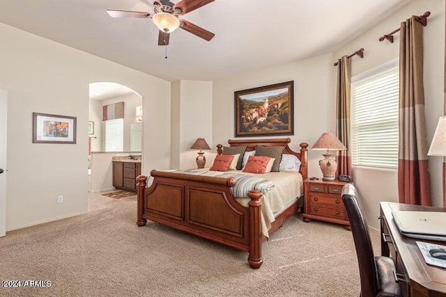 bedroom featuring a ceiling fan, arched walkways, light carpet, and connected bathroom