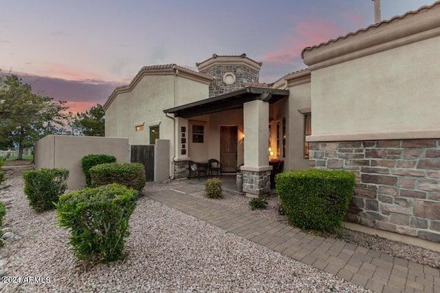 back of house at dusk with stone siding and stucco siding