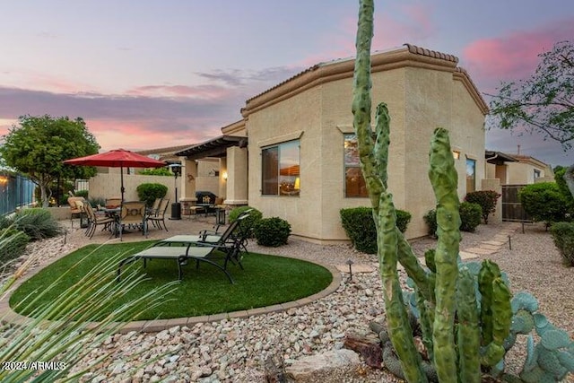 back of house at dusk with a patio area, fence, and stucco siding