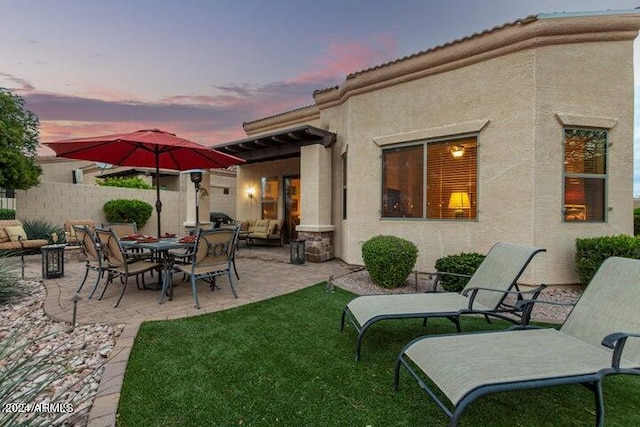 back of property at dusk featuring a patio area, fence, a lawn, and stucco siding