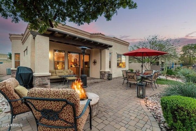 patio terrace at dusk featuring an outdoor living space with a fire pit, area for grilling, fence, and cooling unit