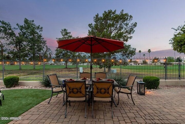 patio terrace at dusk with outdoor dining space, fence, and a lawn