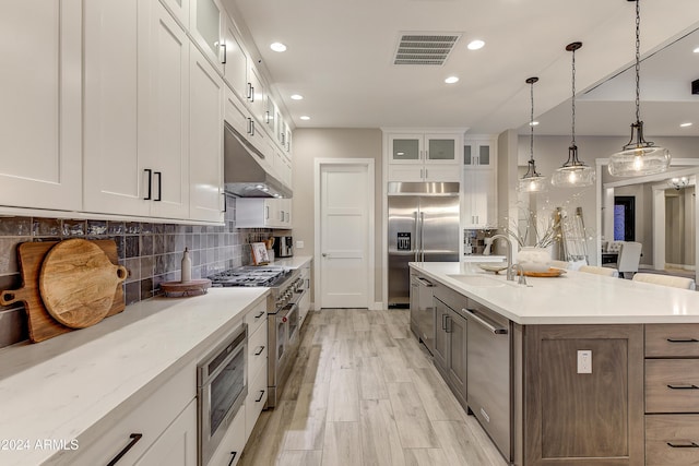 kitchen with pendant lighting, high quality appliances, sink, an island with sink, and white cabinetry