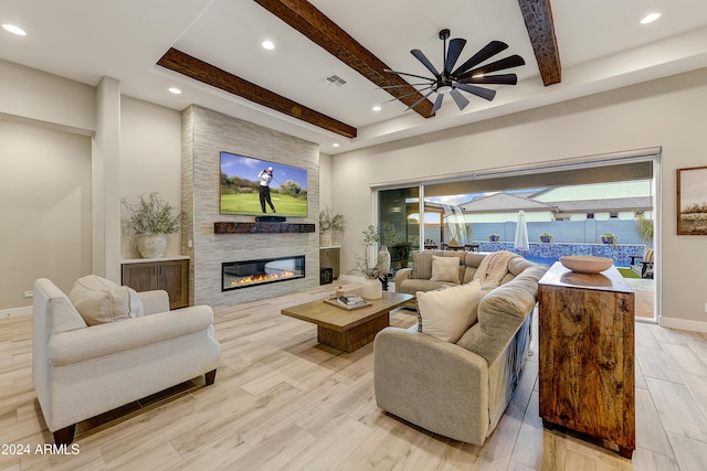 living room with beam ceiling, a large fireplace, light hardwood / wood-style flooring, and ceiling fan