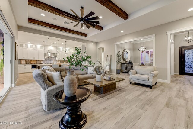 living room featuring beam ceiling, a raised ceiling, light hardwood / wood-style flooring, and ceiling fan with notable chandelier