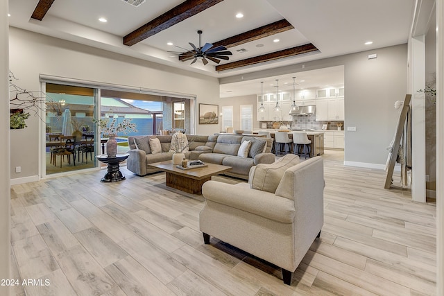 living room with a tray ceiling, ceiling fan, light hardwood / wood-style flooring, and beamed ceiling