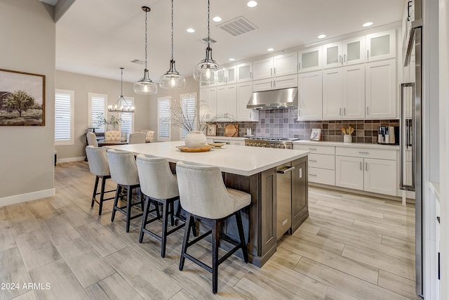 kitchen featuring white cabinets, light hardwood / wood-style floors, an island with sink, and hanging light fixtures