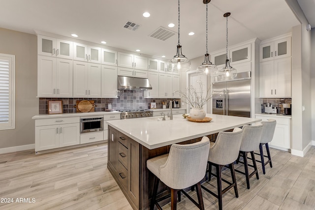 kitchen featuring decorative backsplash, appliances with stainless steel finishes, a center island with sink, decorative light fixtures, and white cabinets