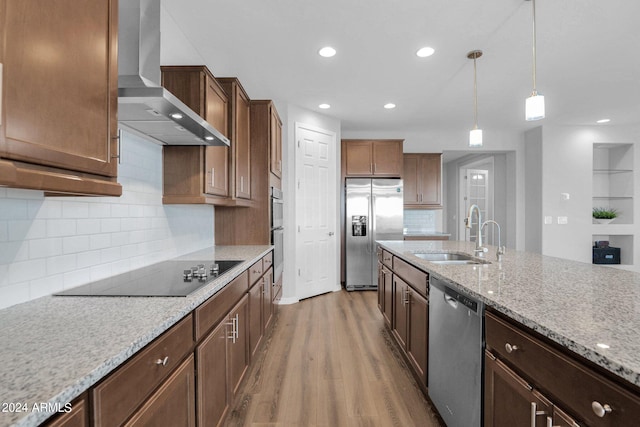 kitchen featuring appliances with stainless steel finishes, pendant lighting, wood-type flooring, sink, and wall chimney range hood