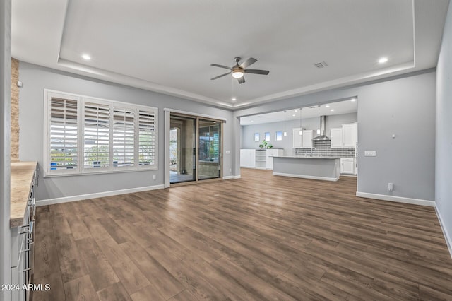 unfurnished living room featuring ceiling fan, dark hardwood / wood-style flooring, and a tray ceiling