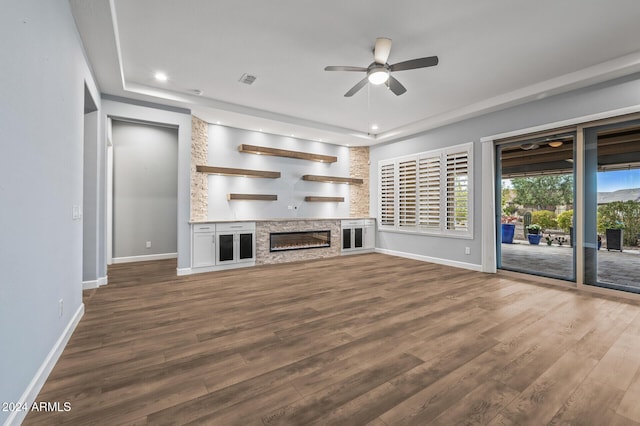 unfurnished living room featuring wood-type flooring, a raised ceiling, a stone fireplace, and ceiling fan