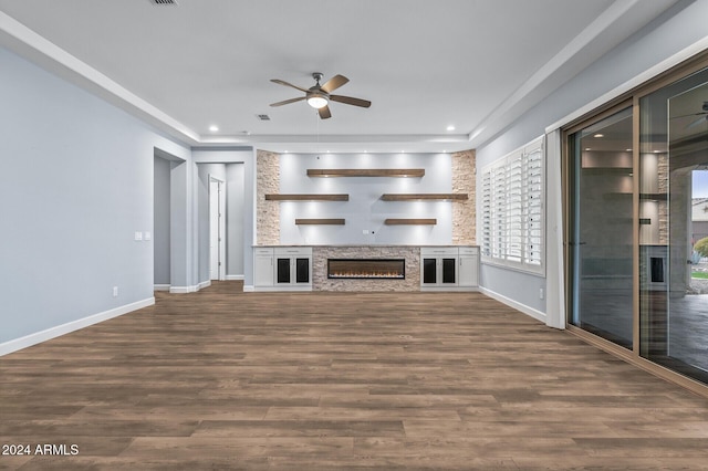 unfurnished living room with ceiling fan, a stone fireplace, and dark wood-type flooring