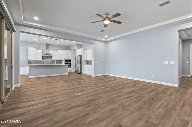 unfurnished living room with dark hardwood / wood-style floors, ceiling fan, and a tray ceiling