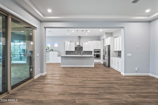 kitchen with white cabinetry, hanging light fixtures, wall chimney range hood, a center island with sink, and appliances with stainless steel finishes