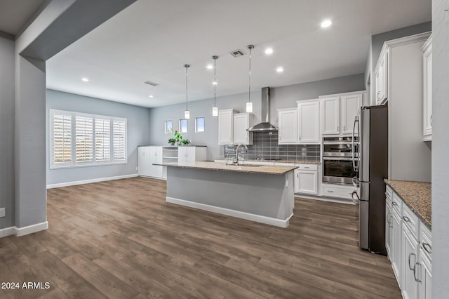 kitchen with a center island with sink, white cabinets, wall chimney exhaust hood, light stone counters, and stainless steel appliances