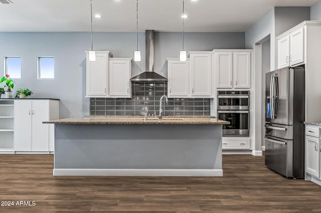 kitchen featuring wall chimney range hood, backsplash, decorative light fixtures, white cabinets, and appliances with stainless steel finishes