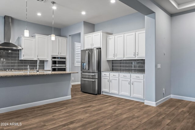 kitchen featuring white cabinetry, wall chimney exhaust hood, stainless steel appliances, tasteful backsplash, and decorative light fixtures