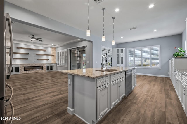 kitchen featuring ceiling fan, dark hardwood / wood-style floors, an island with sink, decorative light fixtures, and light stone counters