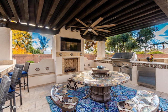 view of patio / terrace with an outdoor fireplace, exterior bar, a grill, area for grilling, and ceiling fan