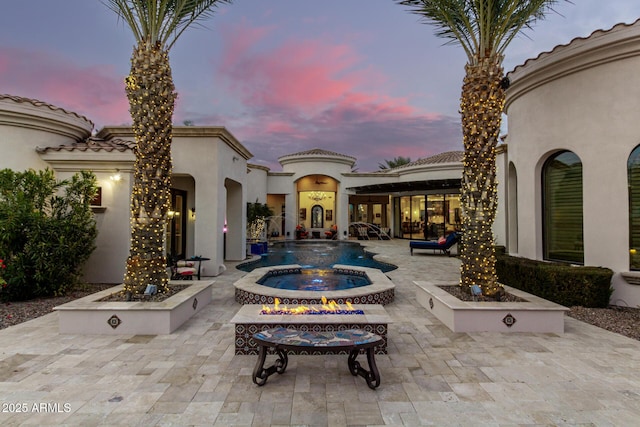 pool at dusk with an in ground hot tub, pool water feature, and a patio area