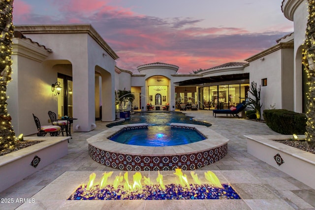 pool at dusk featuring an in ground hot tub, a patio, and an outdoor fire pit