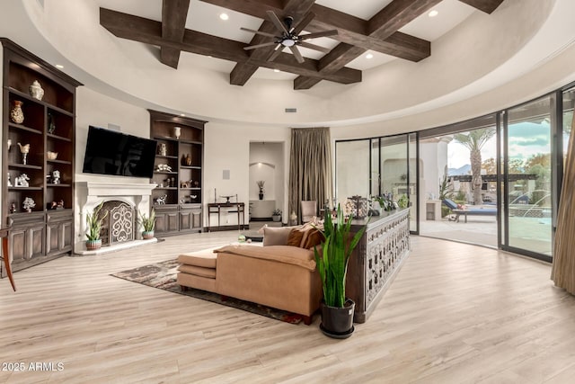 living room with coffered ceiling, a towering ceiling, beamed ceiling, and light wood-type flooring