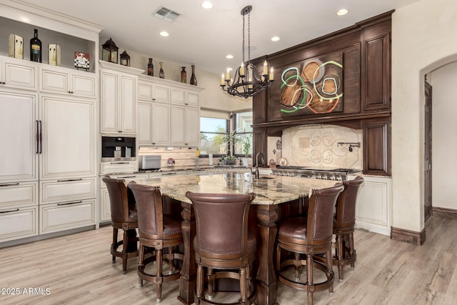 kitchen featuring an island with sink, light stone countertops, oven, and decorative backsplash