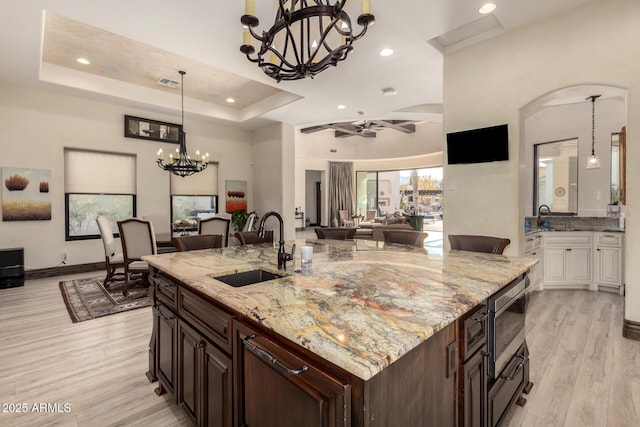 kitchen with a tray ceiling, white cabinetry, sink, light hardwood / wood-style floors, and dark brown cabinetry