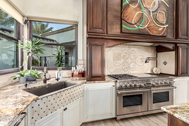 kitchen with sink, double oven range, light hardwood / wood-style floors, light stone countertops, and decorative backsplash