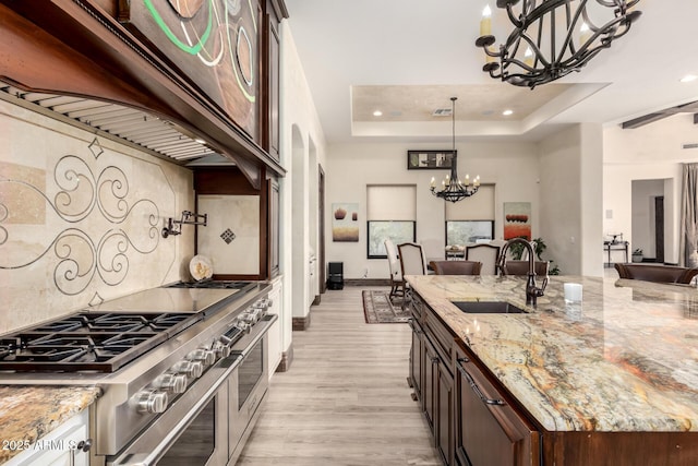 kitchen featuring sink, light stone counters, a chandelier, a tray ceiling, and range with two ovens