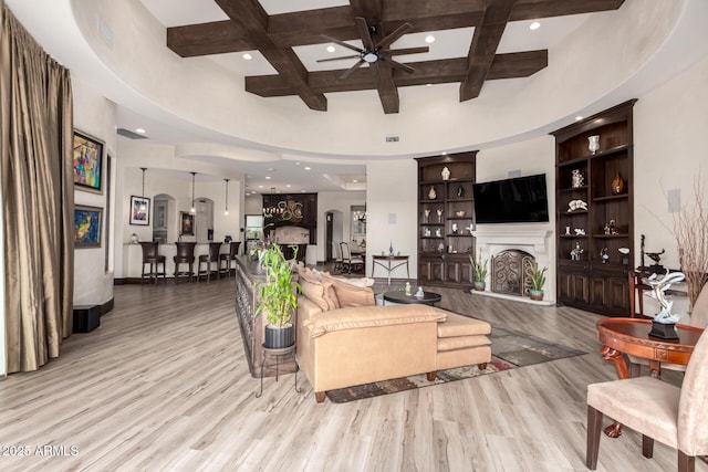 living room with ceiling fan, beam ceiling, a high ceiling, coffered ceiling, and light wood-type flooring