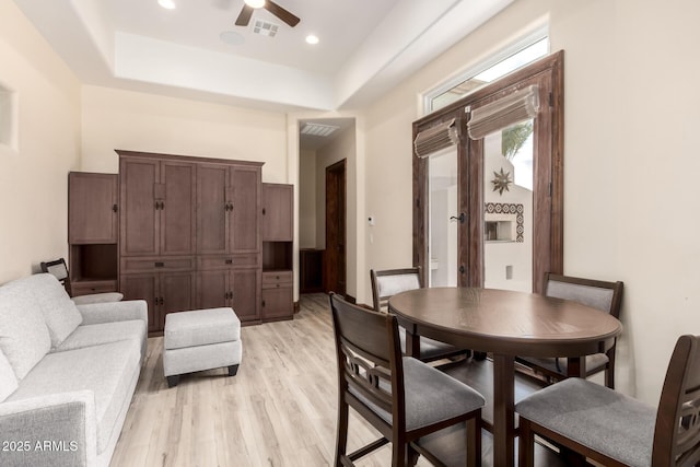 dining room featuring ceiling fan, a towering ceiling, light hardwood / wood-style floors, and a tray ceiling