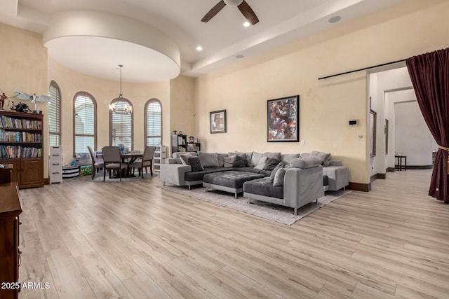 living room with a towering ceiling, ceiling fan, and light hardwood / wood-style flooring