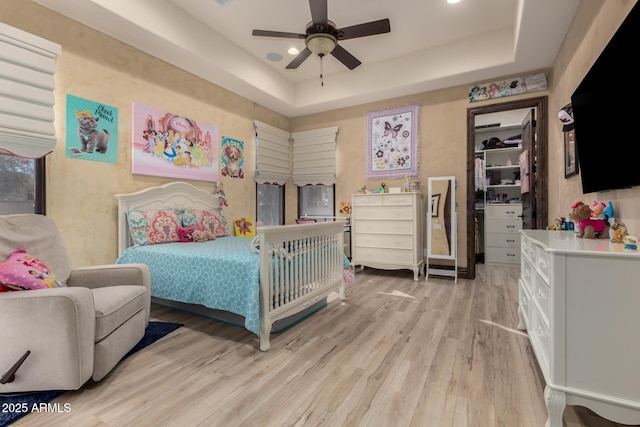 bedroom with light hardwood / wood-style flooring, a raised ceiling, and ceiling fan