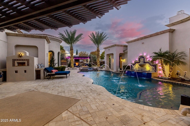 pool at dusk featuring exterior fireplace, a patio area, and pool water feature