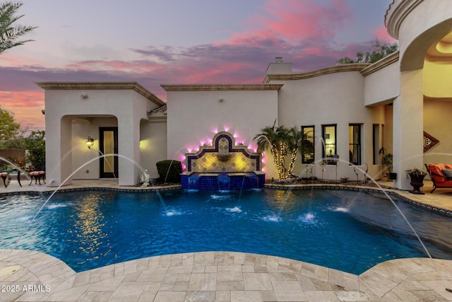 pool at dusk with pool water feature and a patio area