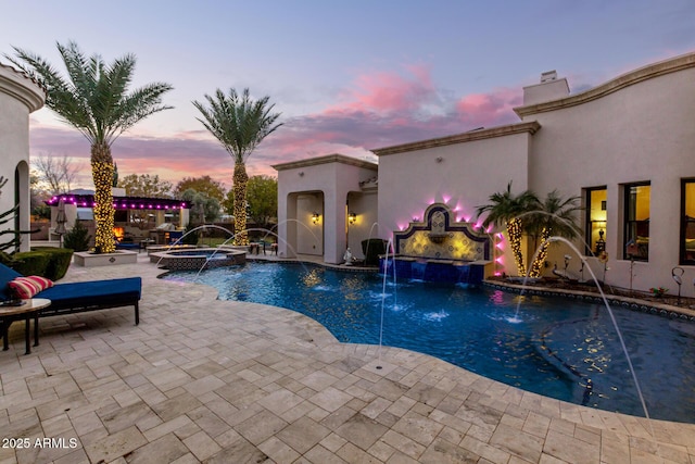 pool at dusk with a patio, pool water feature, and an in ground hot tub