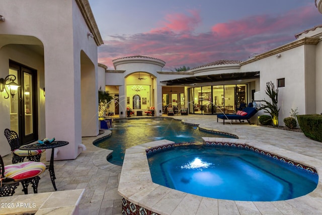 pool at dusk featuring an in ground hot tub, pool water feature, and a patio area